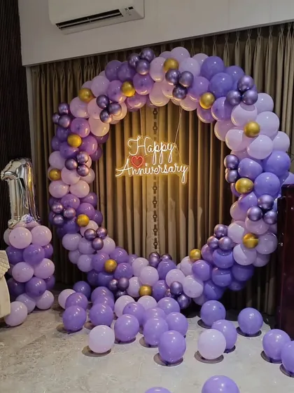 A beautiful circular balloon arch in shades of purple for a first anniversary. The setup is completed with a "Happy Anniversary" neon sign in the center.