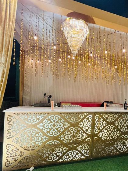 A glamorous gold bar setup, with an intricate laser-cut front panel and a canopy of hanging gold strings and Edison bulbs.
