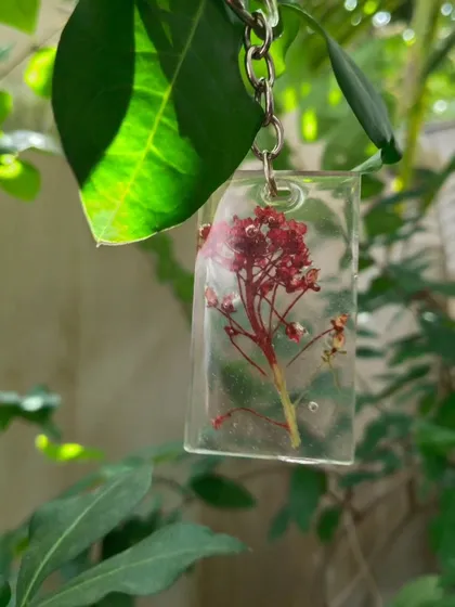 The real flower keychain hanging outdoors, with the sunlight filtering through the leaves behind it.
