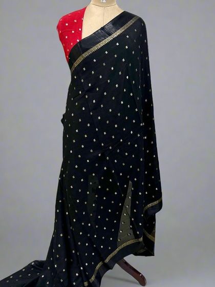 A classic black Chinon saree with a satin border and delicate gold and silver motifs. This piece is displayed on a mannequin with a contrasting red blouse, showing a timeless and elegant party look.