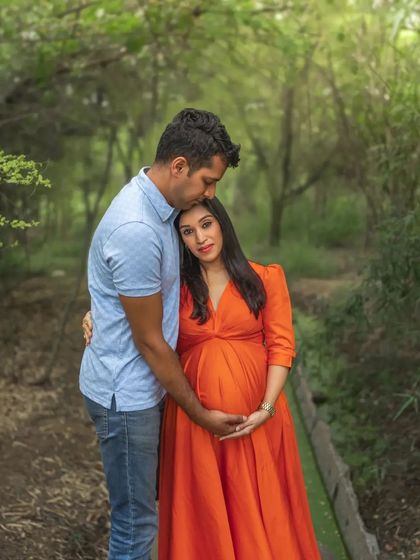 A duplicate of ID 31, this tender outdoor portrait shows a husband gently kissing his wife's head as they both cradle her belly, surrounded by the soft greenery of the woods.
