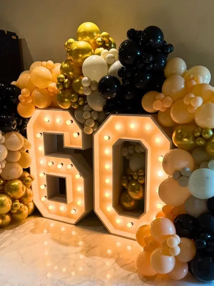 Celebrating a 60th birthday in style with giant, 4-foot tall marquee numbers. The numbers are framed by a dense balloon garland in a classic black, gold, and white color scheme for a timeless look.