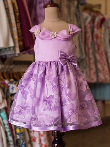 This lavender organza dress is detailed with floral embroidery and delicate flower accents on the collar. It's a sweet, whimsical design for a little one with a big imagination.