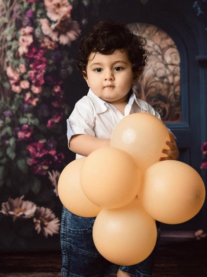 Holding a bunch of balloons, this toddler is ready to celebrate his milestone.