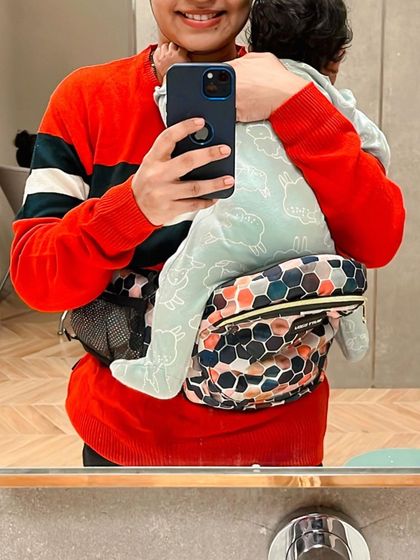 A close-up mirror selfie showing the details of the Buttbaby carrier. It's a product I genuinely love and recommend to other moms.