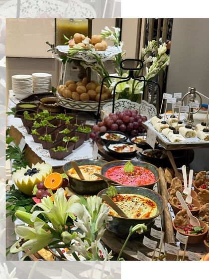 Our grazing tables are a true work of art. This setup features a beautiful assortment of appetizers, dips, and fresh fruits, decorated with white lilies for an elegant touch.