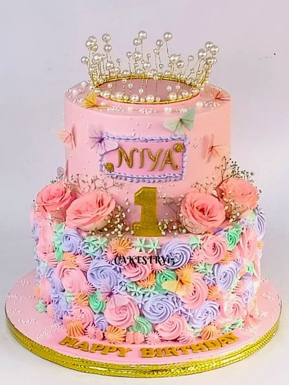A royal two-tier tiara princess cake for a first birthday. This 5kg pineapple cake is decorated with multi-colored rosettes, real flowers, and a sparkling crown topper.