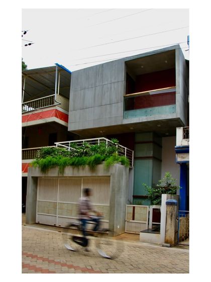 The exterior of the "Boxed In House" presents a bold, concrete form to the street, with carefully placed openings and a green terrace. The design balances the need for privacy with a contemporary architectural statement.