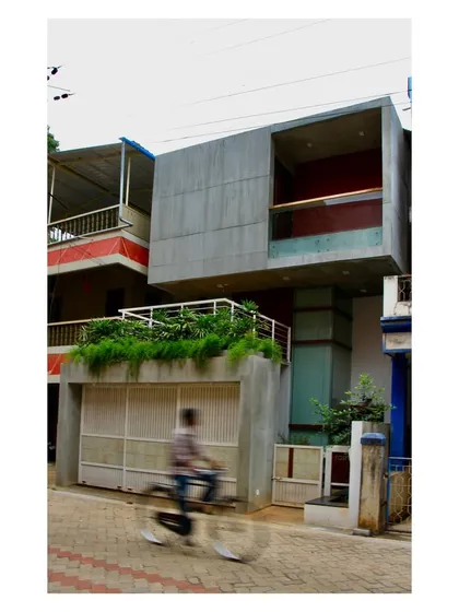 The exterior of the "Boxed In House" presents a bold, concrete form to the street, with carefully placed openings and a green terrace. The design balances the need for privacy with a contemporary architectural statement.