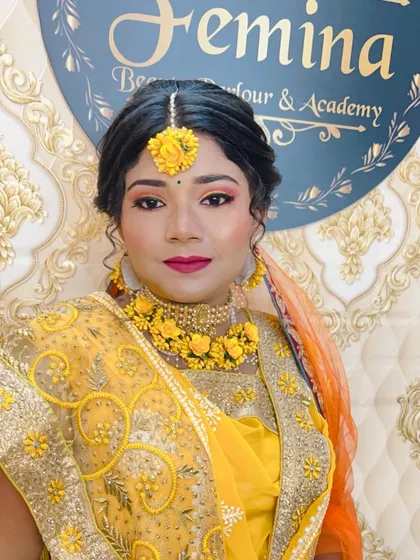 A front-facing portrait of the Haldi bride. Her makeup is kept bright and radiant, with a magenta lip color that stands out beautifully against the yellow of her outfit and floral jewelry.