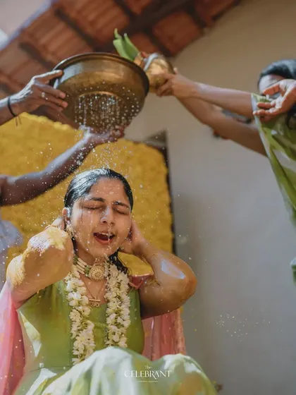 A traditional moment during a Haldi ceremony. The bride is showered with holy water against a backdrop made entirely of bright yellow marigolds, a classic and auspicious choice for this event.