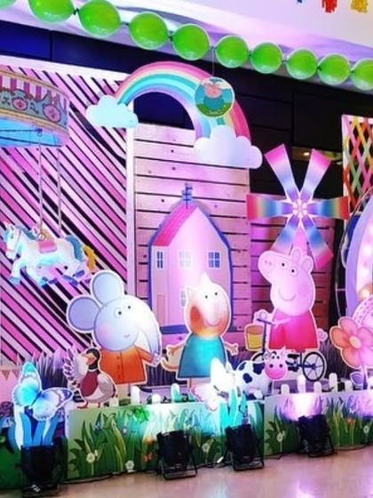 A large and elaborate stage setup for the Peppa Pig party, featuring a carousel, a windmill, and multiple character cutouts against a colorful backdrop.