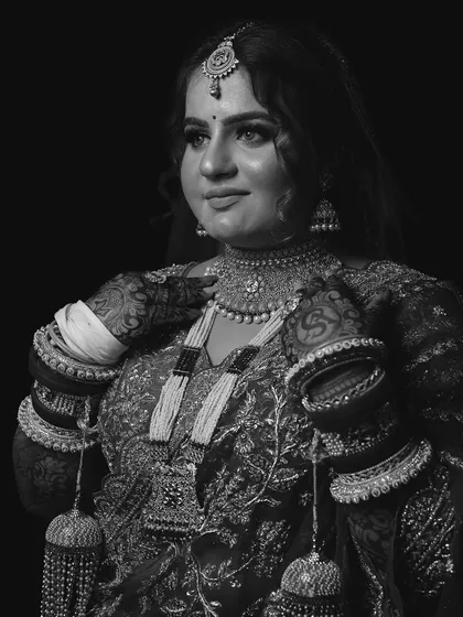 A classic black and white portrait against a dark background, emphasizing the intricate details of the bridal jewelry and outfit.