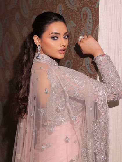 A modern take on the saree. This look, with its unique jacket blouse and soft pink hue, is paired with a dramatic smokey eye and a chic ponytail.