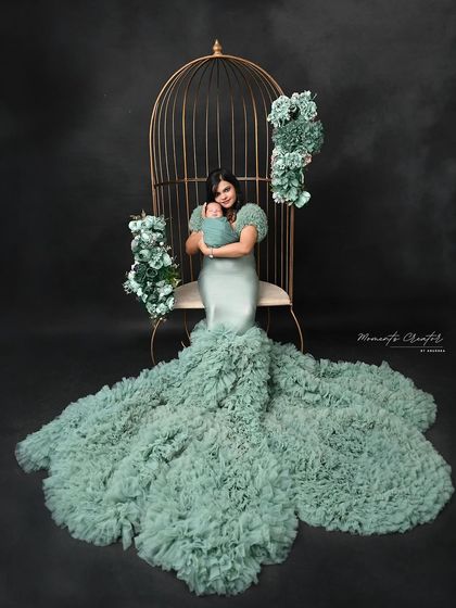 An ethereal portrait of a mother and her newborn. Seated in a golden cage prop adorned with flowers, this image is a unique and artistic take on a mother-child photo.
