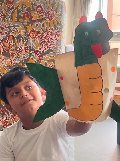 A young boy proudly holds up the dragon paper bag puppet he made. It's so rewarding to see kids excited about their own creations.