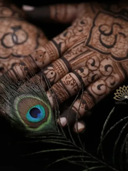 This artistic shot highlights the delicate details of an engagement mehndi. The design incorporates the couple's initials and intertwined rings, beautifully framed by a peacock feather, symbolizing grace and love.