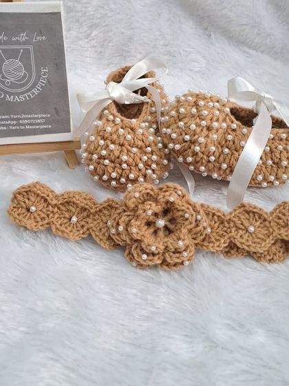 This elegant brown and white baby set is perfect for a neutral-themed gift. The booties are decorated with tiny pearls and a satin ribbon, and the matching headband features a beautiful crochet flower.