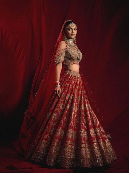 A full-length shot of a majestic red bridal lehenga. The makeup is designed to be both timeless and striking, ensuring the bride looks like royalty on her big day.