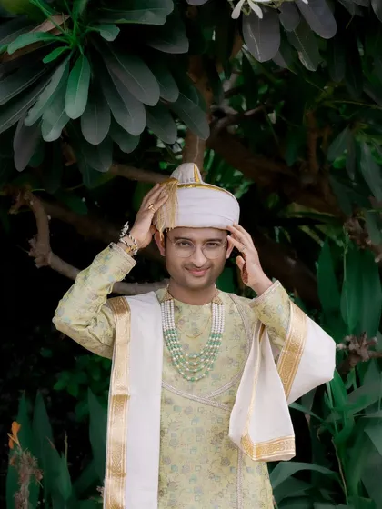 A candid portrait of the groom adjusting his turban (pheta), a classic getting-ready shot from a Maharashtrian wedding.