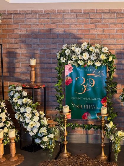 For this 35th birthday, we created a welcoming entrance against a rustic brick wall. A personalized sign was framed with lush white flowers, with more arrangements cascading down modern stands, blending rustic and elegant styles.