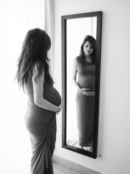 A moment of reflection. Seeing your changing body in the mirror is a powerful part of the pregnancy journey, captured here in a thoughtful black and white portrait.