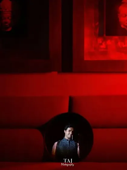 A highly creative and conceptual shot of the groom, framed within a circular cutout of a red sofa. A truly unique and artistic portrait.