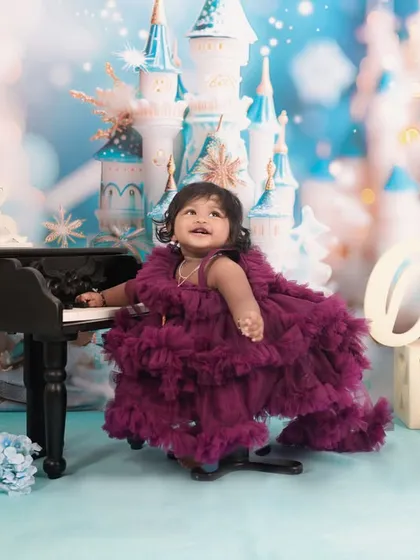 A magical first birthday with a 'Frozen' theme. This little princess is all smiles at her piano in front of a dreamy ice castle backdrop.