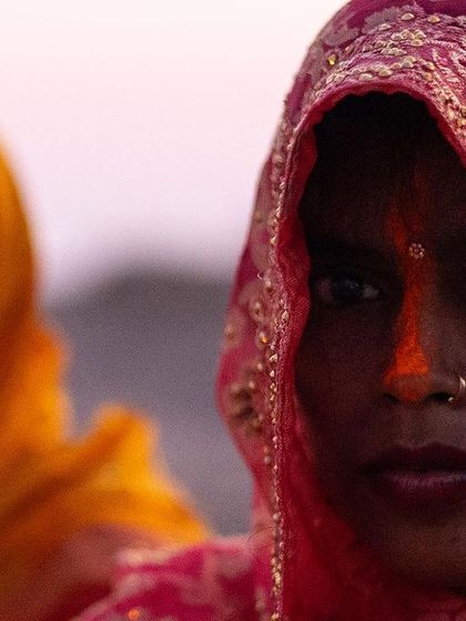 A close-up portrait of two women during Chhath, their faces marked with the traditional orange sindoor. Their direct gaze speaks of profound faith and endurance.