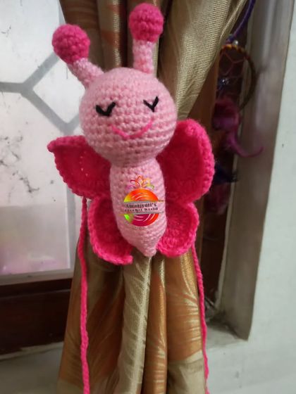 A sweet pink butterfly curtain tie, perfect for adding a whimsical touch to a child's bedroom or nursery. The details in the wings and body are all carefully crocheted.