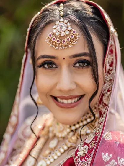 A simple, elegant close-up that captures the bride's happy smile. The makeup is minimal and natural, focusing on clean skin and a simple red bindi.