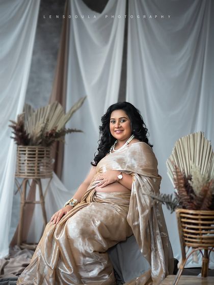 A beautiful seated portrait that highlights the intricate details of the saree and the radiant smile of the mother-to-be.
