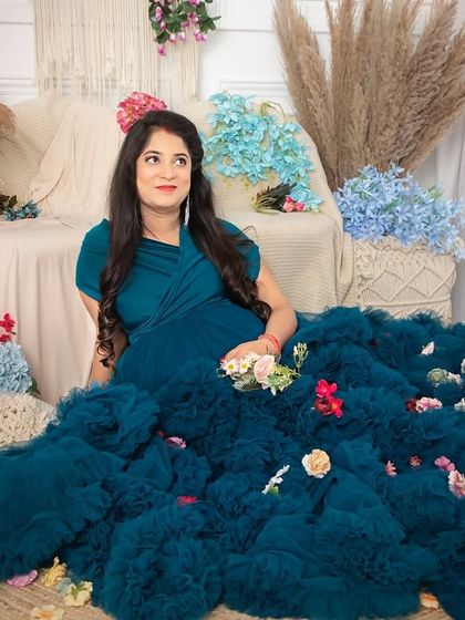 A serene portrait of a mom-to-be nestled in a sea of flowers and soft fabrics. She wears a beautiful teal gown, creating a peaceful and dreamy atmosphere.