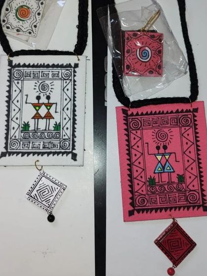 Two variations of the hand-painted Warli art fabric necklace, one on a white base and one on pink. These are lightweight and perfect for bulk orders as return gifts.