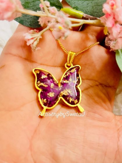 Holding the delicate butterfly pendant, filled with deep red rose petals and sparkling gold leaf.