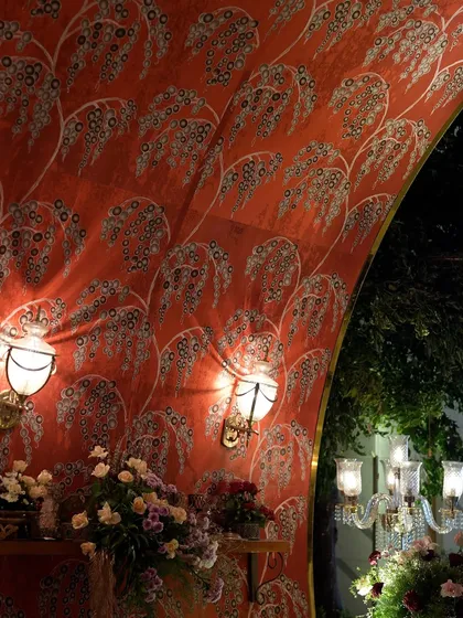The entrance to this grand reception featured an arched tunnel lined with custom-printed fabric in a rich red hue, illuminated by vintage-style wall sconces for a dramatic effect.