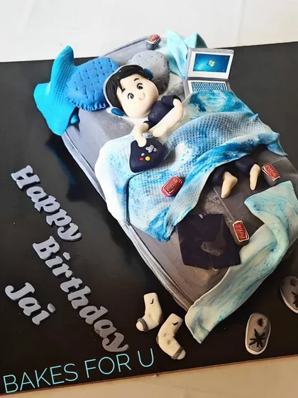 A fun and relatable cake for a teenager, depicting a boy lounging in his messy bed with a laptop, gaming controller, and snacks. Every detail, including the scattered socks, is edible.
