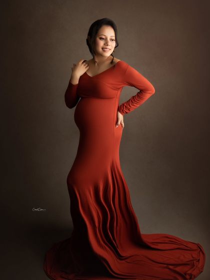 A full-length view of this elegant, long-sleeved orange gown, showing how it drapes beautifully over the baby bump.