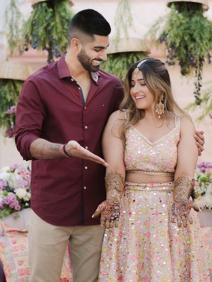 A sweet moment from the Mehendi ceremony. The groom playfully points to the bride's intricate henna, both of them sharing a happy, candid laugh.