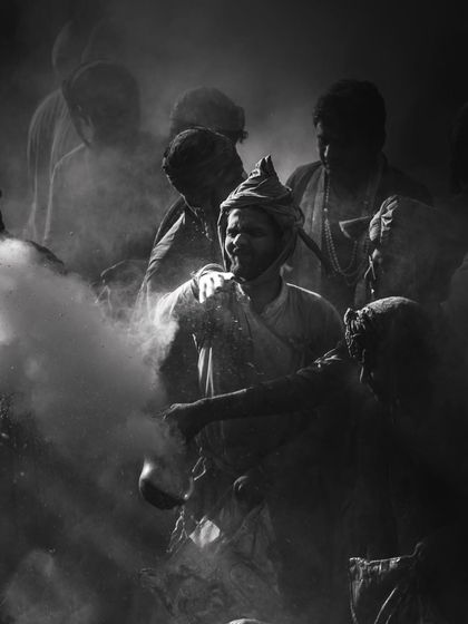 Another monochrome image from Braj ki Holi, focusing on a man's face emerging from the dust and light. The black and white format emphasizes the dramatic textures and emotions.