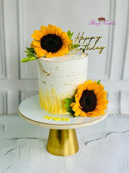 A sunny and cheerful cake for Mom's birthday. This tall cake is decorated with a rustic buttercream texture, gold leaf, and two beautiful, large sunflowers.