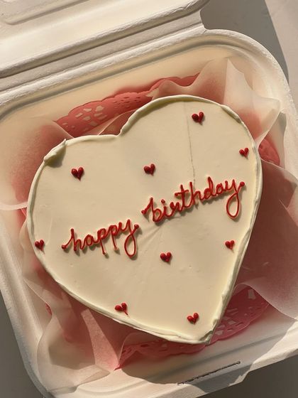 A close-up of a heart-shaped bento cake, showing the smooth buttercream finish and delicate "happy birthday" piping.