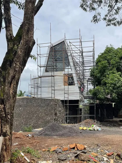 The Karjat residence enveloped in scaffolding, revealing its complex, angular geometry. Even in this raw state, the structure's dynamic relationship with the surrounding trees and landscape is evident.