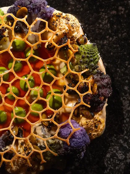 A macro shot of the "Cauli 911" dish, showing the intricate honeycomb detail and colorful vegetables.