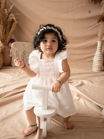 A sweet portrait of a birthday girl in a white dress, posing with a small wooden tricycle.