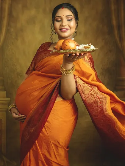 A portrait of pure joy and anticipation. The flowing orange saree and the traditional offering in hand create a vibrant and graceful image, celebrating the beauty of motherhood.