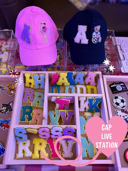 A glimpse of our live cap customization station, showing a variety of colorful chenille initial patches and character designs ready for guests to choose from. This is where the creative fun begins at your event.