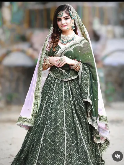 A full-length view of a stunning dark green bridal lehenga with a contrasting pink dupatta. This is a great choice for a winter wedding or reception.