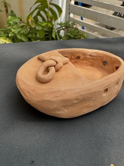 A small, rustic terracotta bowl with a knotted handle, sculpted by Varun. It has a wonderfully earthy and ancient feel to it.
