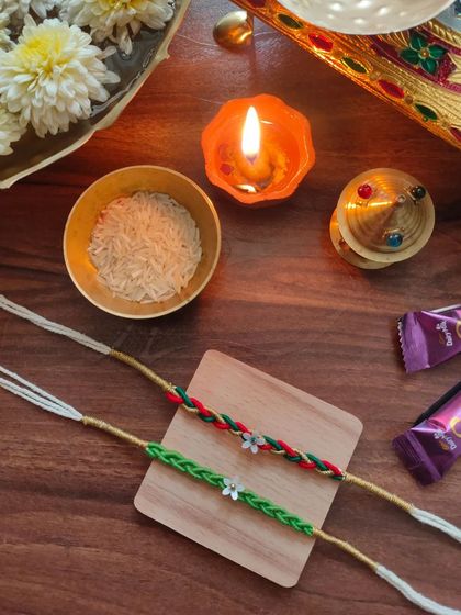 These braided rakhis are a unique option for the festival. They are available in a green braid and a red-and-green braid, each with a small floral charm.